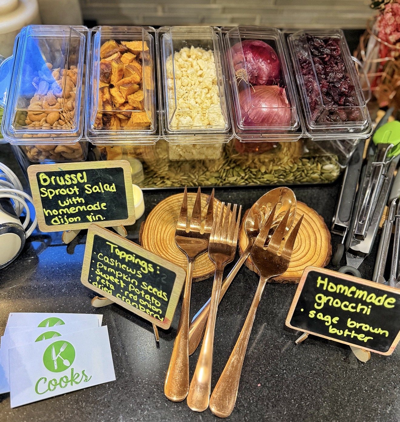 Build-your-own Brussels sprout salad bar with toppings, gold serving forks, and homemade gnocchi sign