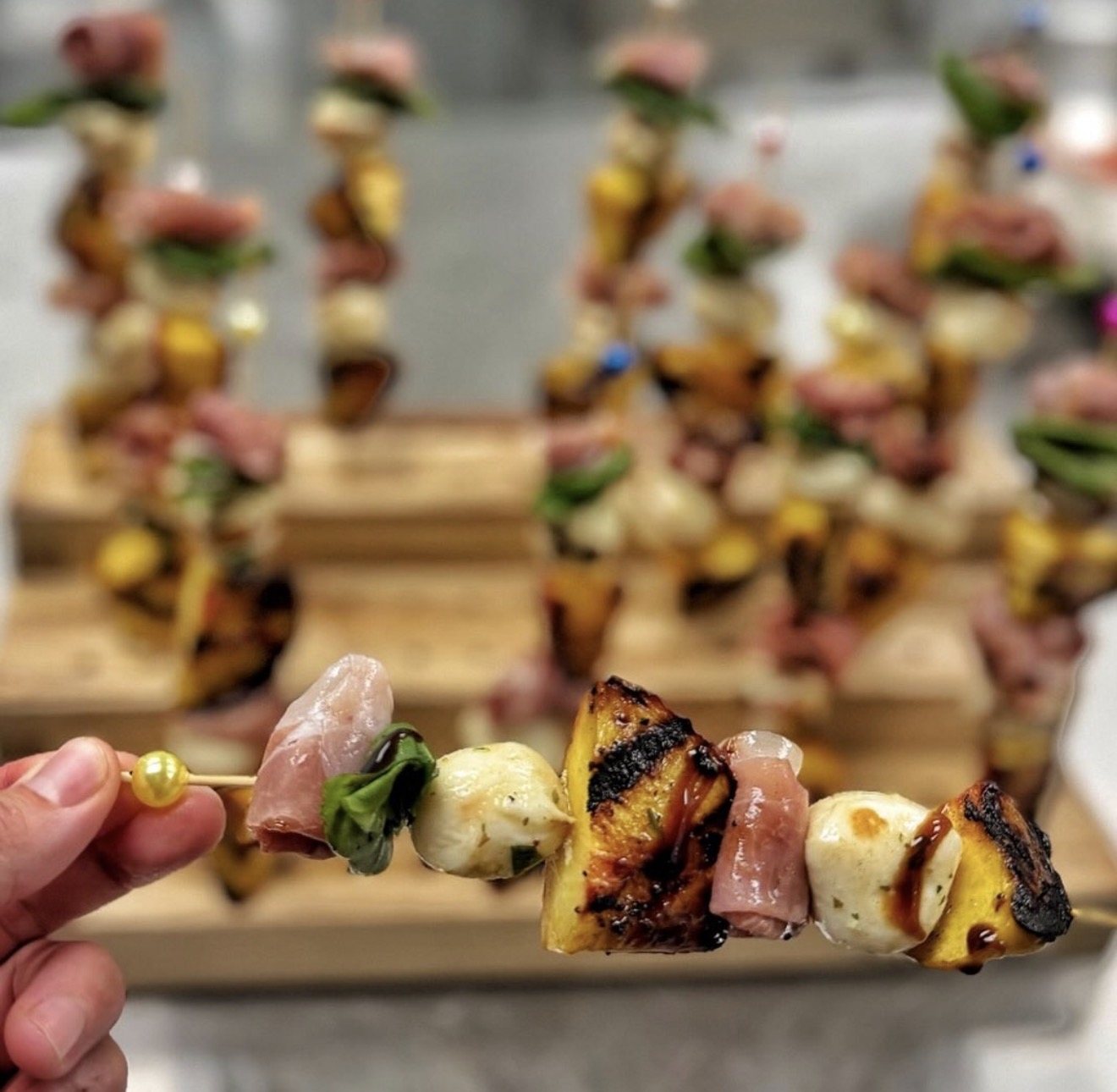 Close-up of a prosciutto, mozzarella, and grilled pineapple skewer from a K Cooks display