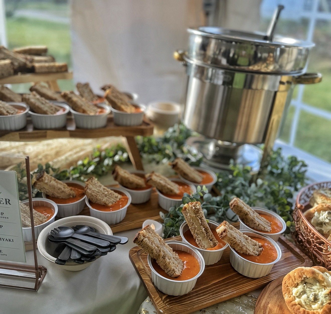 Tomato soup cups with mini grilled cheese on a tiered display beside a soup warmer