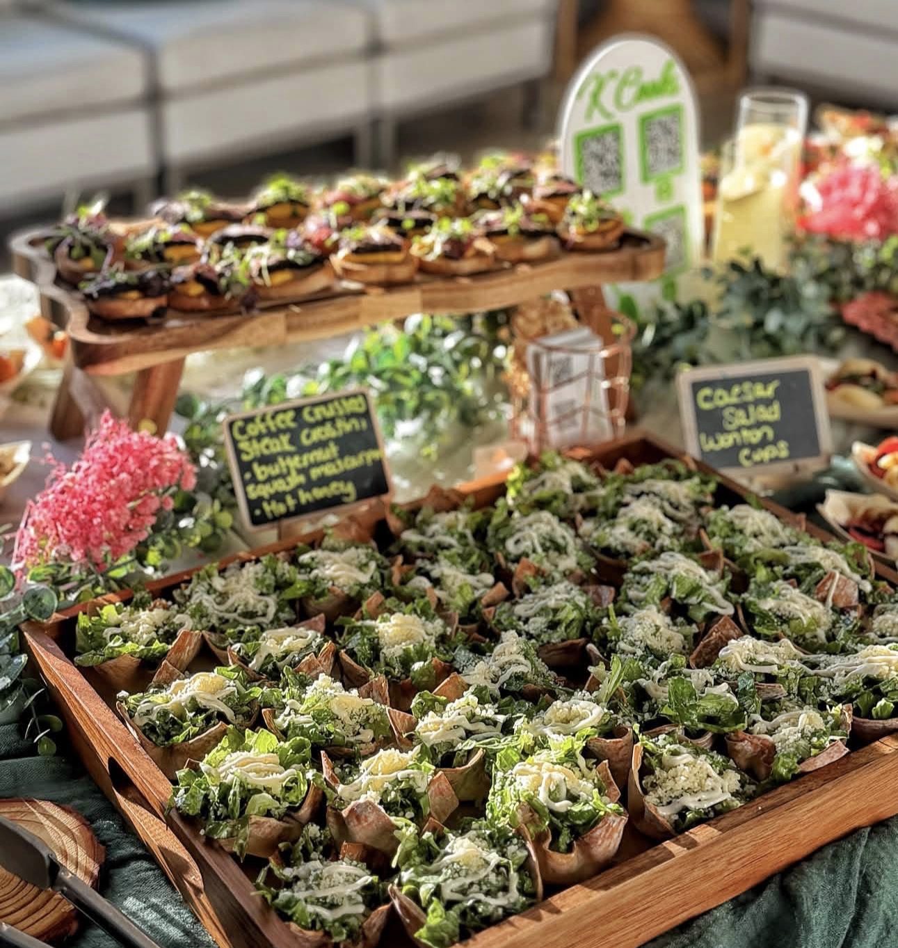 Tiered display of individual Caesar salad cups with chalkboard labels and pink flowers