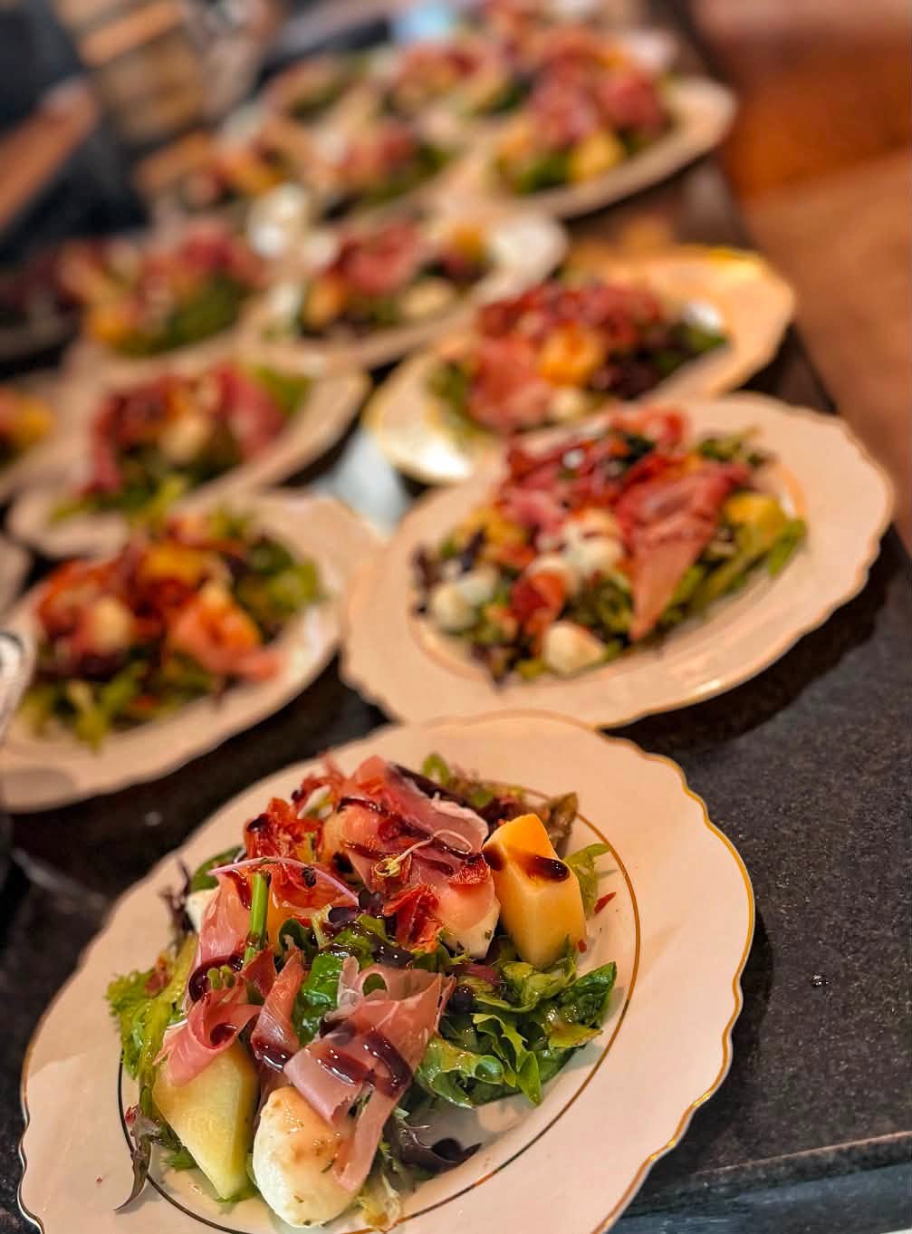 Rows of plated salads with prosciutto, melon, and mozzarella