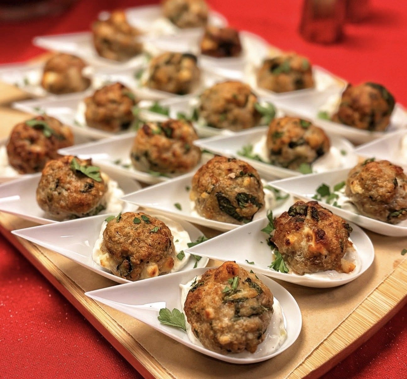 Herb-topped meatballs served in individual white spoons on a wooden tray