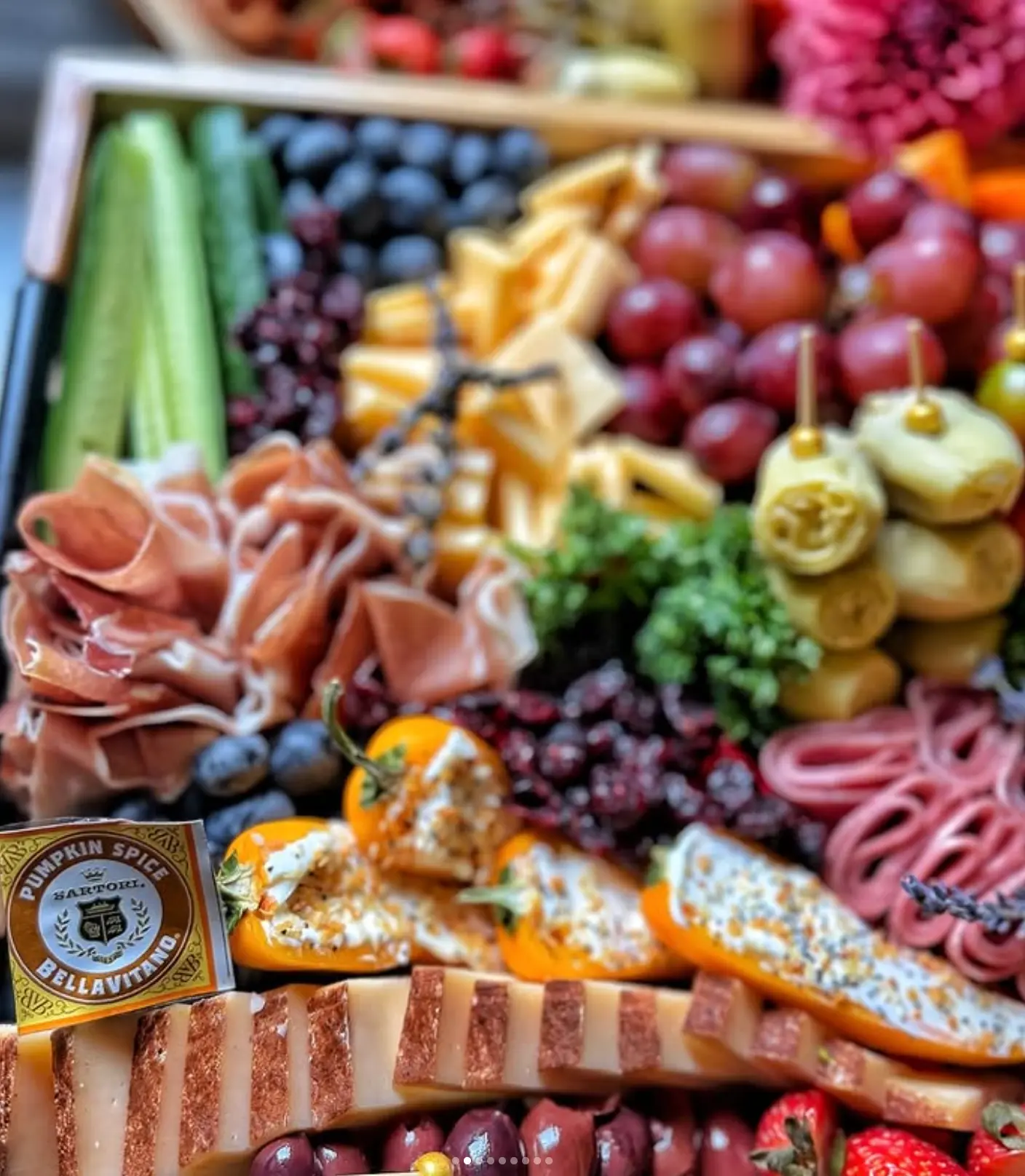 Colorful grazing board with prosciutto, cheeses, grapes, and stuffed peppers
